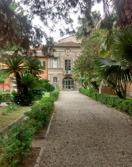 Pathway leading to historic building at Orto Botanico, Palermo, surrounded by lush greenery.
