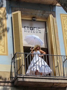 Woman in white dress with umbrella on balcony of Erotic Museum, Barcelona.