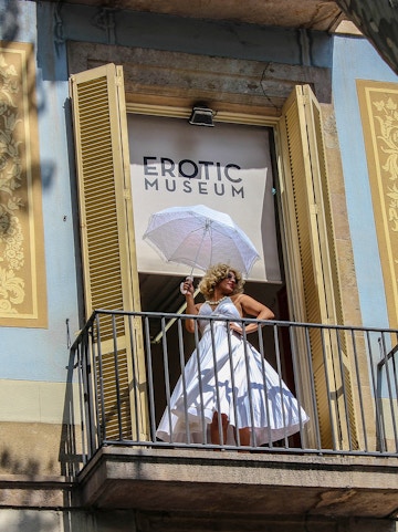 Woman in white dress with umbrella on balcony of Erotic Museum, Barcelona.