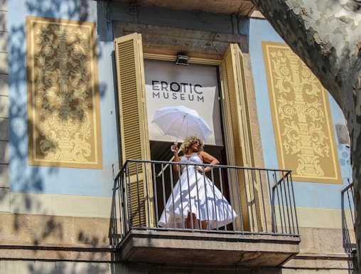 Woman in white dress with umbrella on balcony of Erotic Museum, Barcelona.