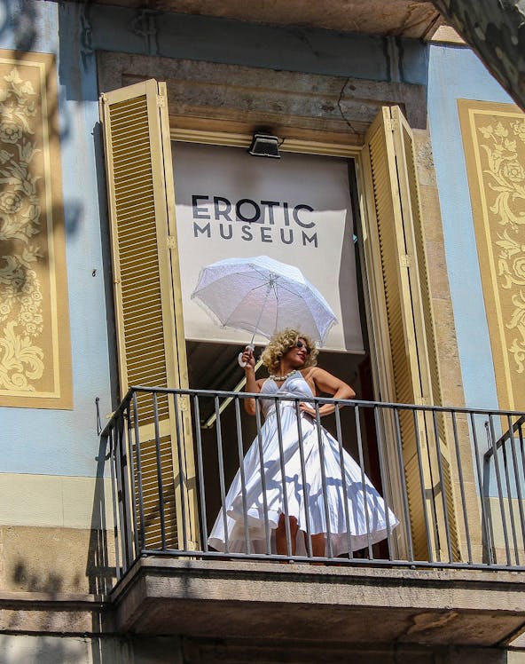 Woman in white dress with umbrella on balcony of Erotic Museum, Barcelona.