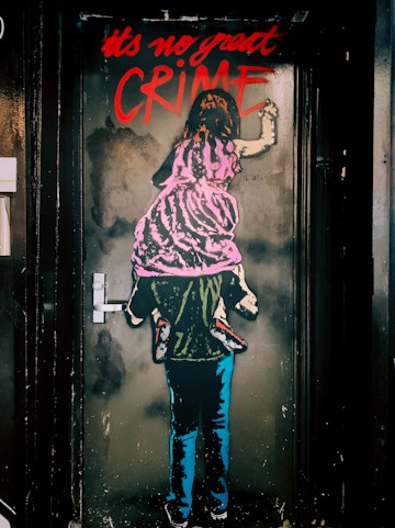 Street art of a child on shoulders writing "It's no great crime" in Barcelona's World of Banksy exhibit.