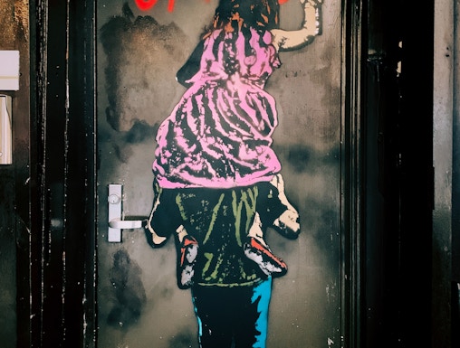 Street art of a child on shoulders writing "It's no great crime" in Barcelona's World of Banksy exhibit.