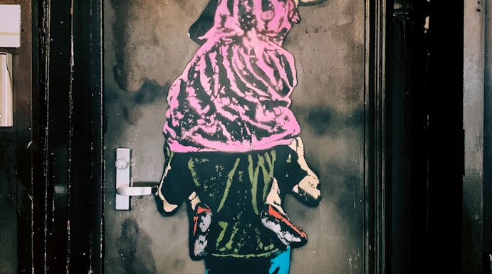 Street art of a child on shoulders writing "It's no great crime" in Barcelona's World of Banksy exhibit.