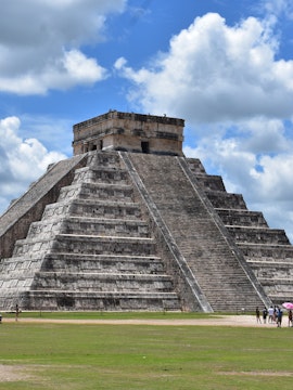 Chichén Itzá pyramid under a cloudy sky with tourists exploring the site in Playa del Carmen.