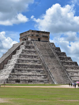 Chichén Itzá pyramid under a cloudy sky with tourists exploring the site in Playa del Carmen.