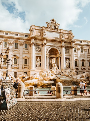 Trevi Fountain in Rome with tourists and street vendor nearby.