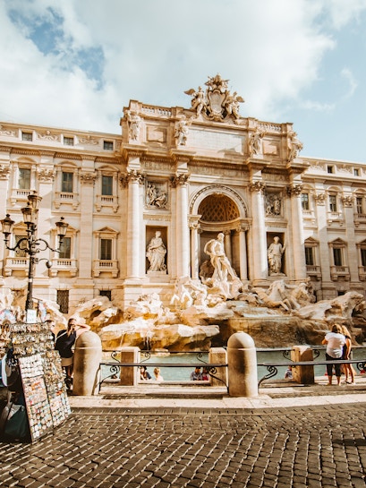 Trevi Fountain in Rome with tourists and street vendor nearby.