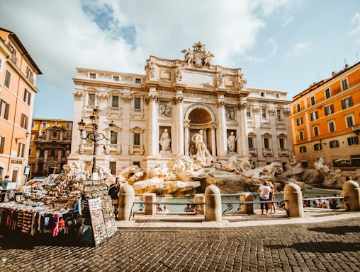 Trevi Fountain in Rome with tourists and street vendor nearby.