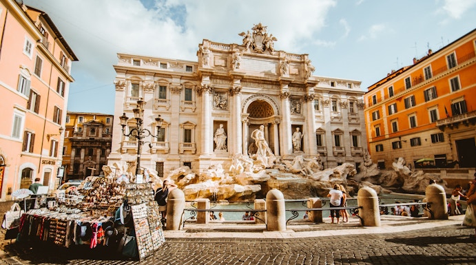 Trevi Fountain in Rome with tourists and street vendor nearby.