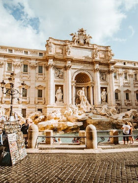 Trevi Fountain in Rome with tourists and street vendor nearby.