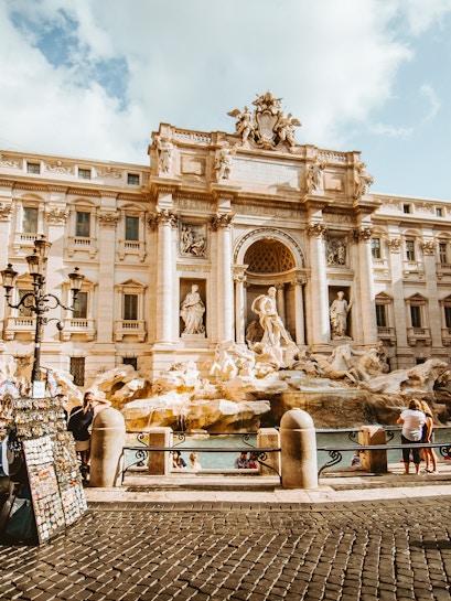 Trevi Fountain in Rome with tourists and street vendor nearby.