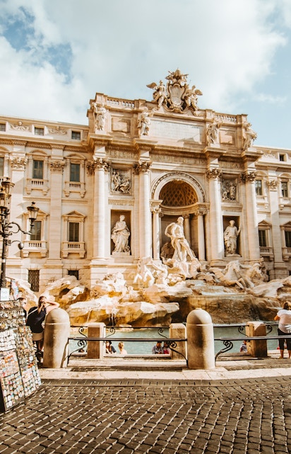 Trevi Fountain in Rome with tourists and street vendor nearby.