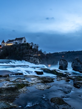 Rhine Falls at dusk with illuminated castle and flowing water, Zurich tour.