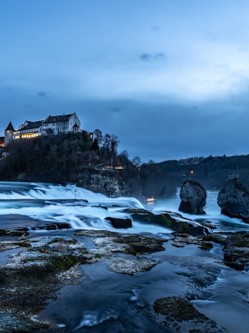 Rhine Falls at dusk with illuminated castle and flowing water, Zurich tour.