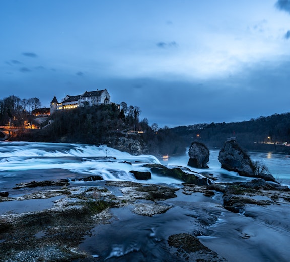 Rhine Falls at dusk with illuminated castle and flowing water, Zurich tour.