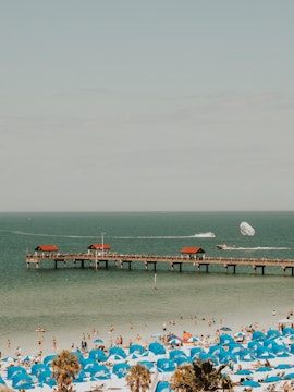 Clearwater Beach with blue umbrellas and pier, parasailing in the distance.