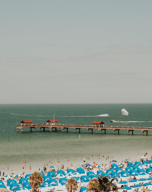Clearwater Beach with blue umbrellas and pier, parasailing in the distance.