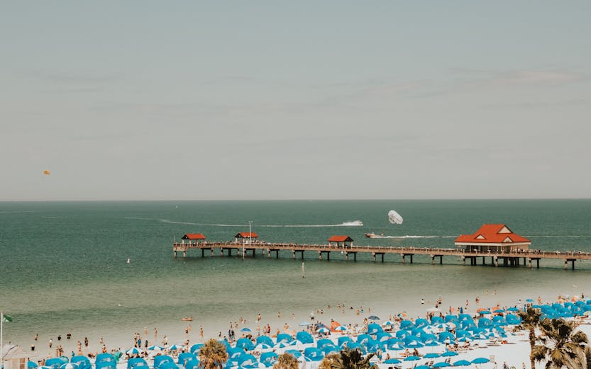 Clearwater Beach with blue umbrellas and pier, parasailing in the distance.