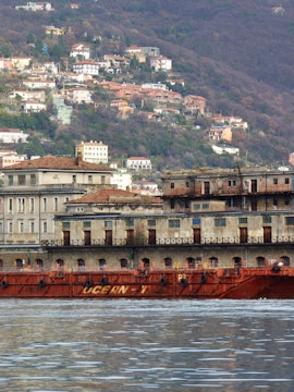 Old port building and ship in Trieste, Italy with hillside houses in the background.