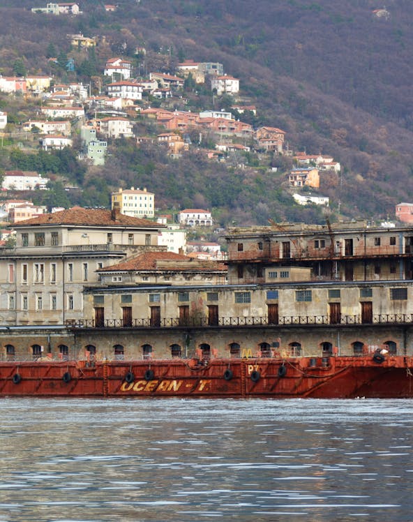 Old port building and ship in Trieste, Italy with hillside houses in the background.