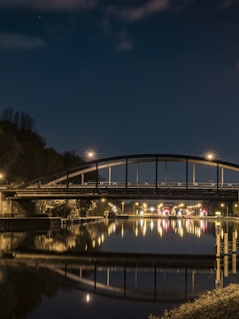 Bridge over a canal at night in Oberhausen, Germany, with streetlights reflecting on the water.