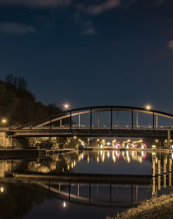 Bridge over a canal at night in Oberhausen, Germany, with streetlights reflecting on the water.