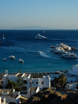 Boats and yachts anchored in the blue waters of Mykonos, Greece, near a coastal village.