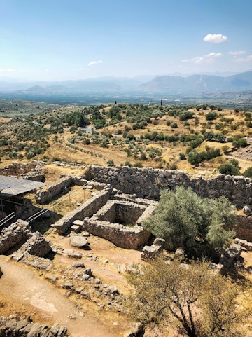 Ancient ruins of Mycenae with olive trees and distant mountains, Greece.