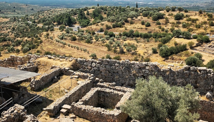 Ancient ruins of Mycenae with olive trees and distant mountains, Greece.