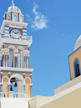 Santorini church bell tower and dome under clear blue sky.