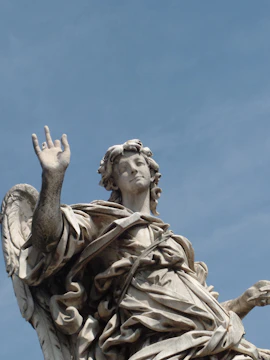Statue of an angel with raised hand against blue sky at Palazzo Merulana, Rome.
