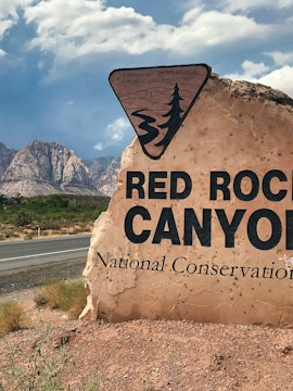 Red Rock Canyon sign with mountains in the background, Nevada desert landscape.