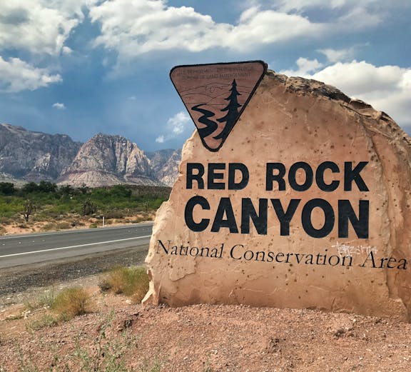 Red Rock Canyon sign with mountains in the background, Nevada desert landscape.