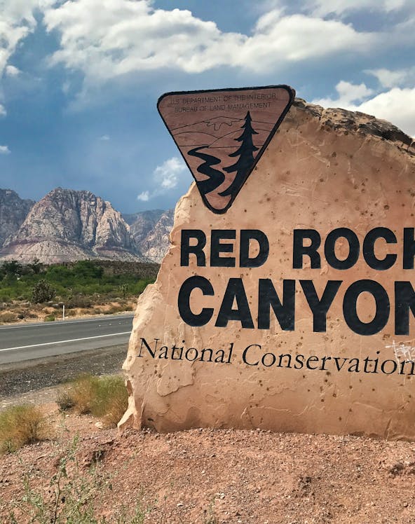 Red Rock Canyon sign with mountains in the background, Nevada desert landscape.