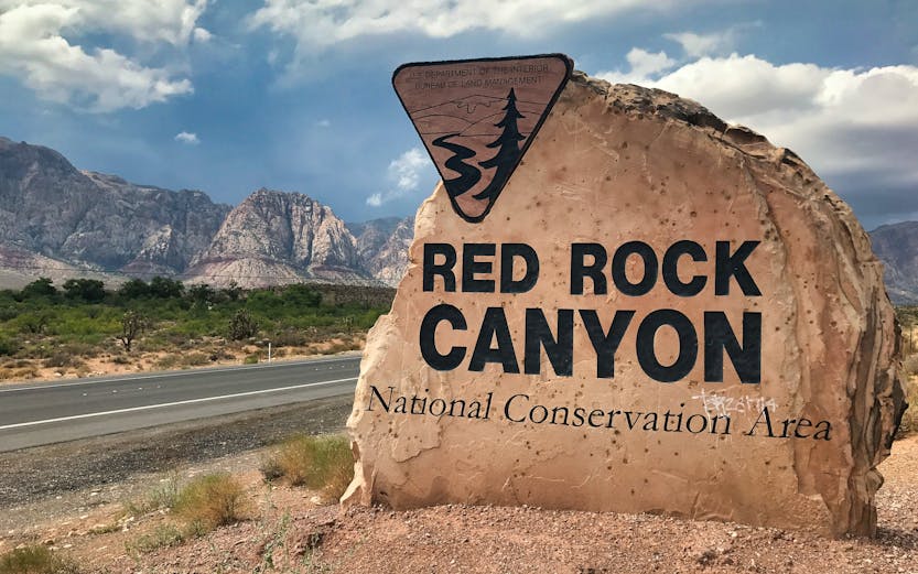 Red Rock Canyon sign with mountains in the background, Nevada desert landscape.