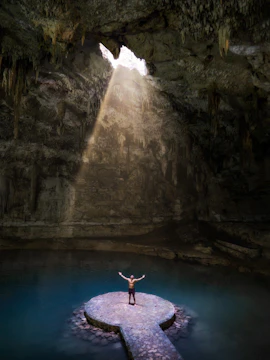 Person standing on a stone platform in Rio Secreto cave with sunlight streaming through an opening.
