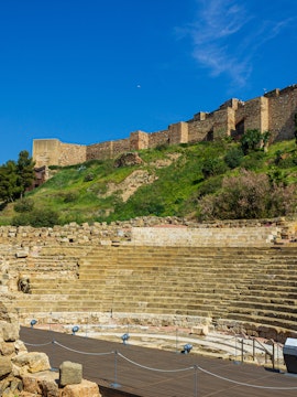 Alcazaba and Roman Theater ruins in Málaga, Spain, with ancient stone seating and fortress walls.