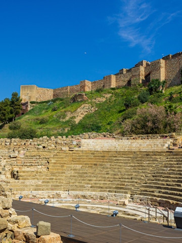 Alcazaba and Roman Theater ruins in Málaga, Spain, with ancient stone seating and fortress walls.