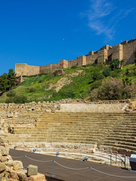 Alcazaba and Roman Theater ruins in Málaga, Spain, with ancient stone seating and fortress walls.