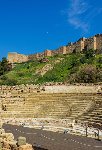 Alcazaba and Roman Theater ruins in Málaga, Spain, with ancient stone seating and fortress walls.