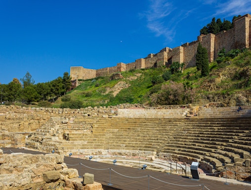 Alcazaba and Roman Theater ruins in Málaga, Spain, with ancient stone seating and fortress walls.