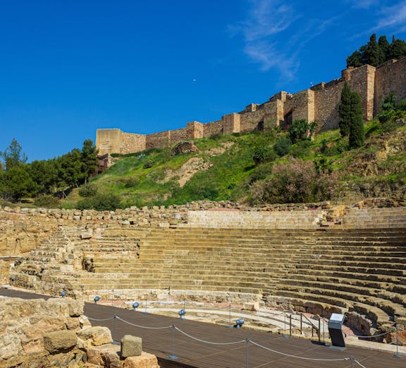Alcazaba and Roman Theater ruins in Málaga, Spain, with ancient stone seating and fortress walls.