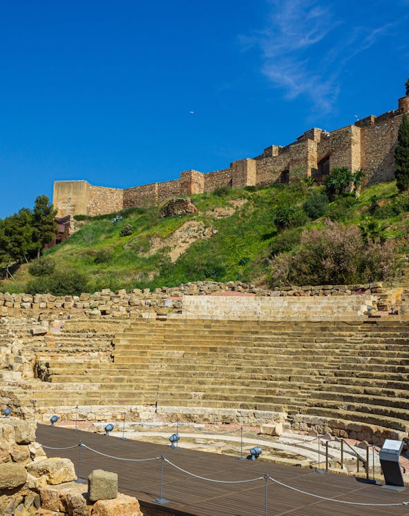 Alcazaba and Roman Theater ruins in Málaga, Spain, with ancient stone seating and fortress walls.