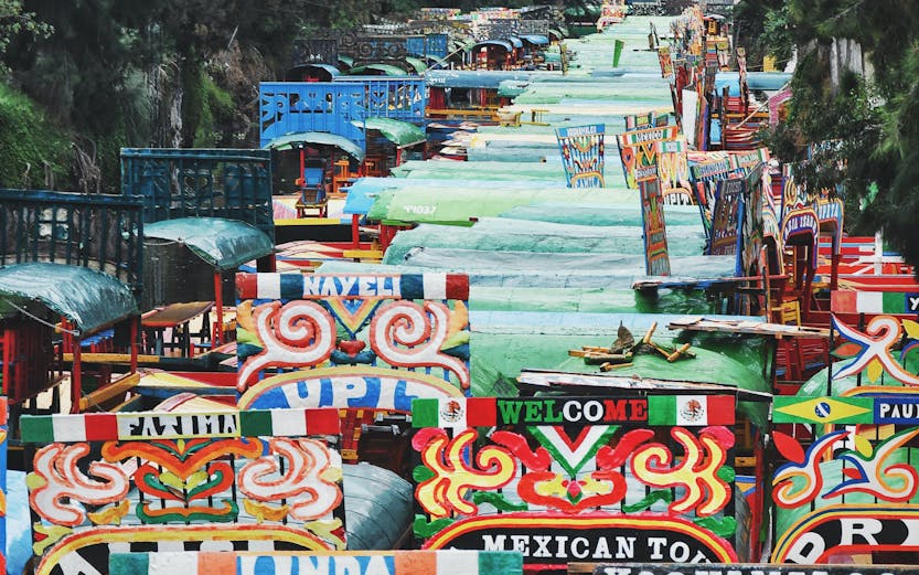 Colorful trajineras on the canal in Xochimilco, Mexico City, surrounded by lush trees.