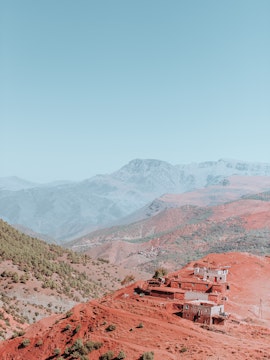 Village on red hills in the Atlas Mountains with distant peaks in the background.
