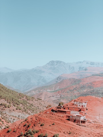 Village on red hills in the Atlas Mountains with distant peaks in the background.
