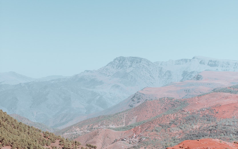 Village on red hills in the Atlas Mountains with distant peaks in the background.