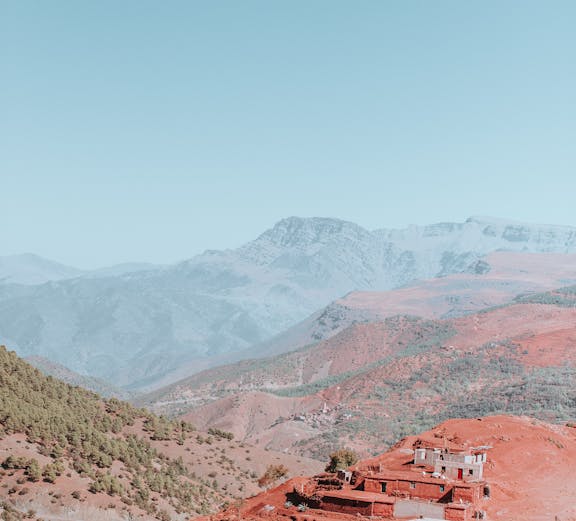 Village on red hills in the Atlas Mountains with distant peaks in the background.