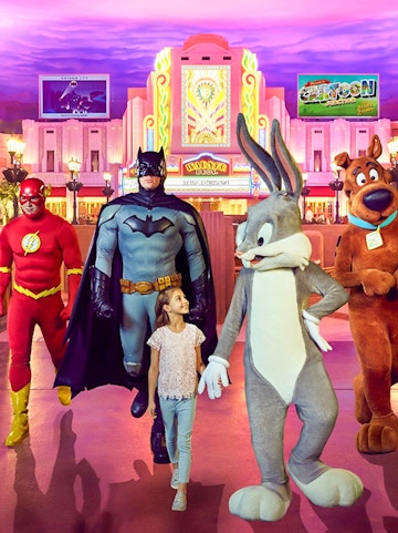 Child walking with Warner Bros characters at Abu Dhabi theme park.